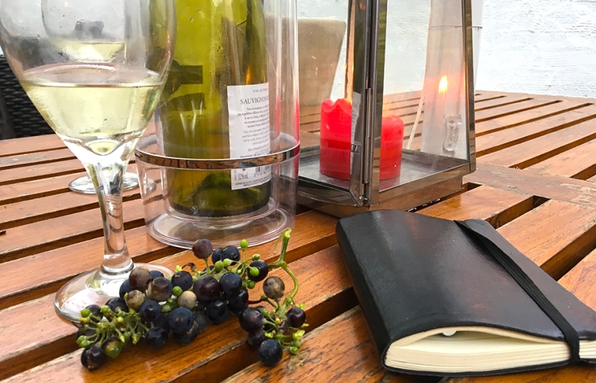 grapes, notebook, white wine half-full glasses on wooden outdoor table