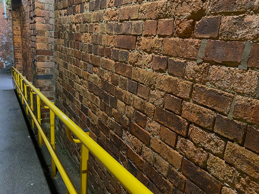 Station ramp: red brick wall, yellow hand rail.